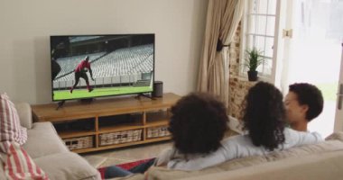 Mutlu bir ailenin evde oturup televizyonda rugby maçı izlemesinin birleşimi. spor, rekabet, eğlence ve teknoloji konsepti dijital olarak oluşturulmuş video.