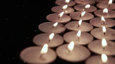 Beyaz kar tanelerinin siyah arka planda yanan çay ışığı mumlarının üzerine düşmesi. kutlama, parti, gelenek ve olay konsepti dijital olarak oluşturulmuş video.