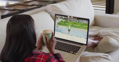 Evde oturmuş, elinde kahve olan bir kadının dizüstü bilgisayardan atlama müsabakalarını izlemesinin birleşimi. spor, rekabet, eğlence ve teknoloji konsepti dijital olarak oluşturulmuş video.