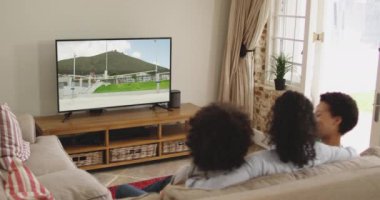 Mutlu bir ailenin evde oturup TV 'de yüksek atlama atletizm izlemesinin birleşimi. spor, rekabet, eğlence ve teknoloji konsepti dijital olarak oluşturulmuş video.