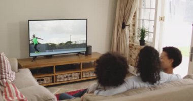 Mutlu bir ailenin evde oturup TV 'de cirit atmasını izlemesinin birleşimi. spor, rekabet, eğlence ve teknoloji konsepti dijital olarak oluşturulmuş video.