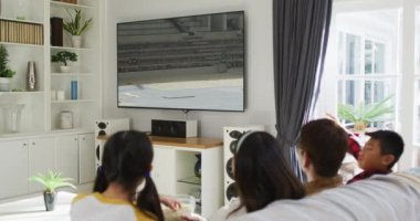 Mutlu bir ailenin evde oturup uzun atlama müsabakalarını izlemesinin birleşimi. spor, rekabet, eğlence ve teknoloji konsepti dijital olarak oluşturulmuş video.