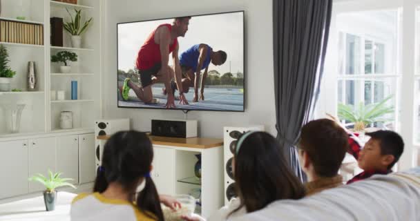 Yhdistelmä Onnellinen Perhe Istuu Kotona Yhdessä Katsomassa Yleisurheilua Käynnissä Televisiossa — kuvapankkivideo