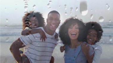 Güneşli bir günde kumsalda gülümseyen Afrikalı Amerikalı ailelerin üzerine damlacıkların animasyonu. Ailenin birlikte boş zaman geçirmesi, dijital olarak oluşturulan video.