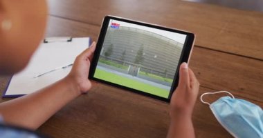Masada maskeyle oturmuş tabletteki atletizm cirit yarışmasını izleyen bir kadın. covid 19 konseptinde dijital olarak üretilen spor, rekabet, eğlence ve teknoloji.