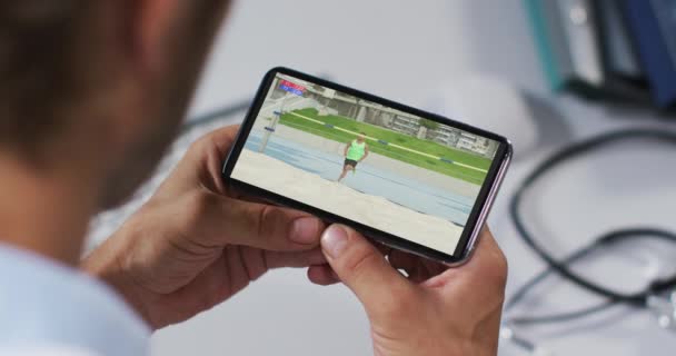 Komposit Dokter Laki Laki Menonton Atletik Lompat Tinggi Acara Smartphone — Stok Video