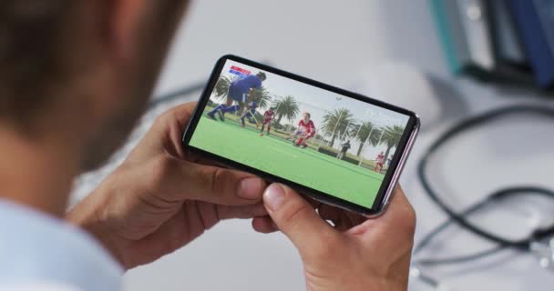 スマートフォンでホッケーの試合を見て男性医師の複合体 スポーツ エンターテイメント テクノロジーの概念をデジタルで生成したビデオ — ストック動画