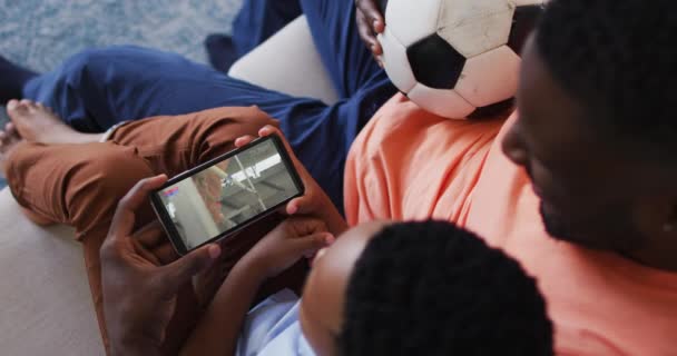 スマートフォンで陸上競技のハイジャンプイベントを見て自宅で父と息子の複合体 スポーツ エンターテイメント テクノロジーの概念をデジタルで生成したビデオ — ストック動画