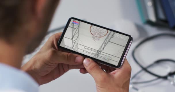 スマートフォンでバスケットボールの試合を見て男性医師の複合体 スポーツ エンターテイメント テクノロジーの概念をデジタルで生成したビデオ — ストック動画