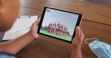 Masada maskeyle oturmuş, tabletten spor müsabakaları seyreden bir kadın. covid 19 konseptinde dijital olarak üretilen spor, rekabet, eğlence ve teknoloji.