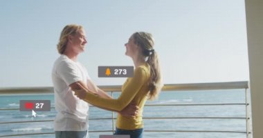 Sosyal medya simgelerinin deniz kenarında kucaklaşan beyaz çift üzerindeki afişlerde canlandırılması. Sosyal medya, dijital arayüz ve bağlantılar konsepti dijital olarak oluşturulmuş video.