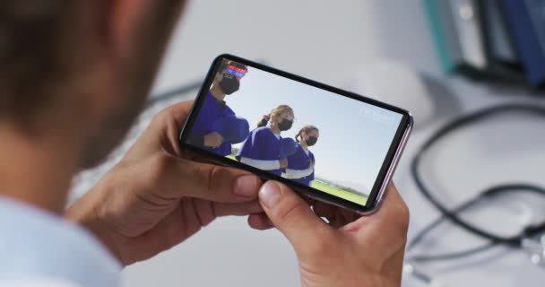 Compuesto Médico Masculino Viendo Partido Béisbol Durante Covid Teléfono Inteligente — Vídeo de stock