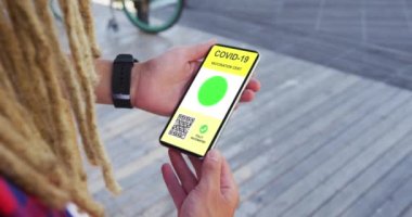 Rastalı bir adam elinde akıllı telefon, elinde komando aşısı sertifikası ve ekrana QR kodu tutuyor. covid 19 salgın sırasında dijital olarak üretilen video sırasında sağlık, yaşam tarzı, seyahat ve teknoloji.