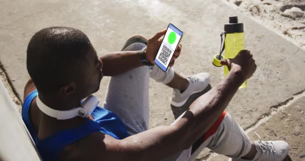 男人坐在街上拿着智能手机 手里拿着绿皮疫苗接种证书 屏幕上有Qr代码 数码视频概念期间的医疗保健 生活方式 旅行和技术 — 图库视频影像