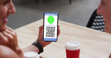 Kafedeki adam, ekranda video aşısı sertifikası ve QR kodu olan akıllı telefonu gösteriyor. covid 19 salgın sırasında dijital olarak üretilen video sırasında sağlık, yaşam tarzı, seyahat ve teknoloji.