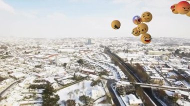 Birden fazla yüz emojisinin dijital bileşimi karla kaplı şehir manzarasının havadan görüntüsüne karşı yüzüyor. Sosyal medya ağı ve teknoloji kavramı