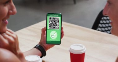 Kafedeki adam, ekranda video aşısı sertifikası ve QR kodu olan akıllı telefonu gösteriyor. covid 19 salgın sırasında dijital olarak üretilen video sırasında sağlık, yaşam tarzı, seyahat ve teknoloji.