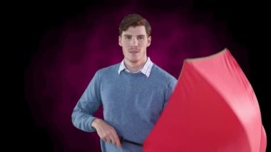 Gülümseyen adam pembe ve siyah arka plana kırmızı şemsiye koyup altına sığınıyor. doğa, hava durumu, koruma ve değişim konsepti dijital olarak oluşturulmuş video.