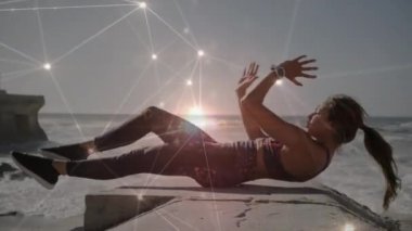 Sahilde karın kası egzersizi yapan beyaz bir kadına karşı parlayan bir bağlantı ağı. Spor, spor ve teknoloji konsepti