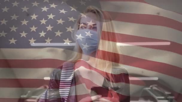 Amerikaanse Vlag Zwaaien Tegen Blanke Vrouw Met Gezichtsmasker Met Smartphone — Stockvideo