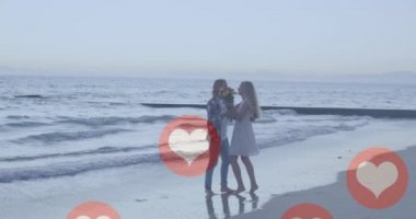 Sahilde öpüşen beyaz bir çifte karşı birden fazla kırmızı kalp ikonu. Sosyal medya ağı ve teknoloji kavramı