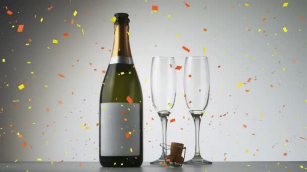 シャンパンボトルの上にコンフェッティが落ち グレーを背景にシャンパングラスが2つ 大晦日のパーティーとお祝いのコンセプト — ストック動画