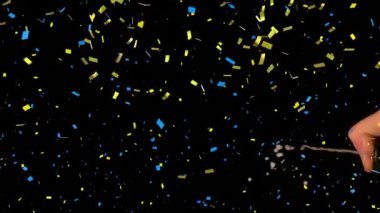 Konfeti, insanın orta kısmından düşüp siyah arka plana şampanya püskürtüyor. Yeni yıl kutlaması ve gece hayatı konsepti