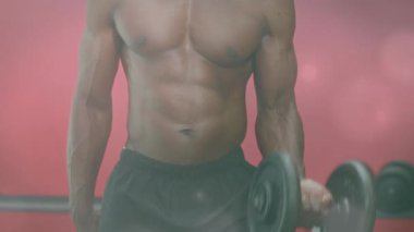 Afrika kökenli Amerikalı formda bir adamın spor salonunda dambıllarla çalışmasına karşı bir ışık lekesi. Spor ve spor teknolojisi kavramı