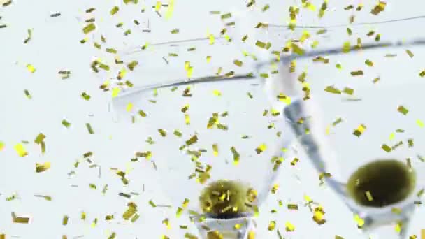 Gouden Confetti Valt Olijven Twee Cocktailglazen Tegen Een Grijze Achtergrond — Stockvideo