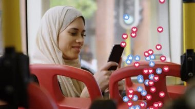 Otobüste akıllı telefon kullanan tesettürlü kadın üzerine düşen sosyal medya simgeleri. küresel sosyal medya, dijital arayüz, teknoloji ve bağlantılar konsepti dijital olarak oluşturulmuş video.