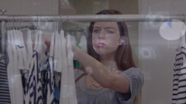 Dükkanda asılı kıyafetlere bakarken akıllı telefon kullanan bir kadının veri işleme animasyonu. moda ve giyim sektörü ve perakende konsepti dijital olarak oluşturulmuş video.