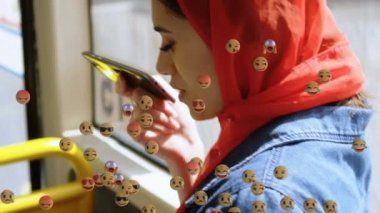 Otobüste akıllı telefon kullanan tesettürlü bir kadının üzerine düşen emojilerin animasyonu. küresel sosyal medya, dijital arayüz, teknoloji ve bağlantılar konsepti dijital olarak oluşturulmuş video.