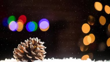 Çam kozalağı ve renkli bokeh üzerine yağan karın animasyonu. Noel, kış, gelenek ve kutlama konsepti dijital olarak oluşturulmuş video.