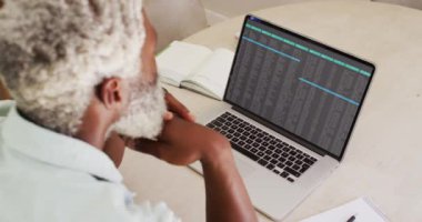 Afrika kökenli Amerikalı bir adam masada oturmuş dizüstü bilgisayardan veri işleme programını izliyor. bilgisayar kodlaması, veri teknolojisi ve dijital arayüz konsepti dijital olarak oluşturulmuş video.