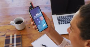 Masada oturan melez kadın ekranda istatistiklerle akıllı telefon kullanıyor. iletişim, veri teknolojisi ve dijital arayüz kavramı dijital olarak oluşturulmuş video.