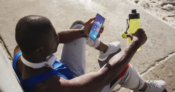 Deportista Afroamericano Sentado Pavimento Usando Smartphone Con Estadísticas Pantalla Comunicación — Vídeos de Stock
