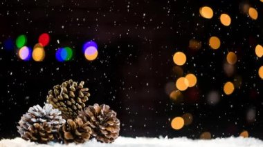 Çam kozalakları ve renkli bokeh üzerine düşen kar animasyonu. Noel, kış, gelenek ve kutlama konsepti dijital olarak oluşturulmuş video.