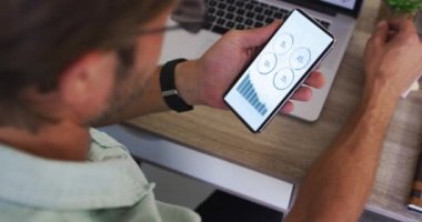 Masada oturan beyaz adam ekranda istatistikleri olan akıllı telefon kullanıyor. iletişim, veri teknolojisi ve dijital arayüz kavramı dijital olarak oluşturulmuş video.