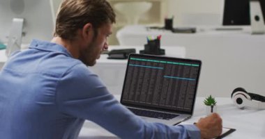 Beyaz bir adam masa başında oturmuş dizüstü bilgisayarını inceliyor ve notlar alıyor. bilgisayar kodlaması, veri teknolojisi ve dijital arayüz konsepti dijital olarak oluşturulmuş video.