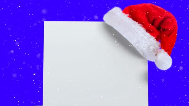 雪の上にコピースペースのあるサンタの帽子と白いカードのアニメーションは青の背景に落ちます クリスマス お祝いのコンセプトをデジタルで — ストック動画