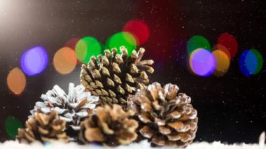 Çam kozalağı ve renkli bokeh üzerine yağan karın animasyonu. Noel, kış, gelenek ve kutlama konsepti dijital olarak oluşturulmuş video.