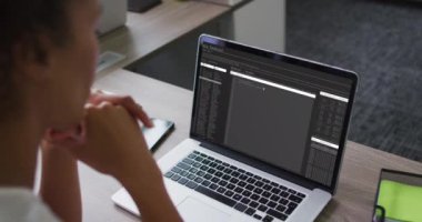 Karışık ırk kadını masada oturmuş dizüstü bilgisayardan veri işleme programını izliyor. bilgisayar kodlaması, veri teknolojisi ve dijital arayüz konsepti dijital olarak oluşturulmuş video.