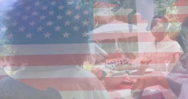 Afro-Amerikan ailesinin bahçede yemek yemesi üzerine Amerikan bayrağının animasyonu. Amerikan vatanseverliği ve bağımsızlık kavramı dijital olarak oluşturulmuş video.