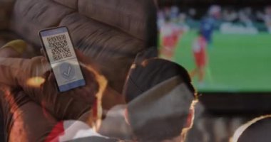 Ekranda QR kodlu bir akıllı telefonu tutan bir kadın arkadaşlarının tezahürat yapmasına ve maç izlemesine karşı. covid-19 aşı sertifikası ve sağlık geçiş kartı