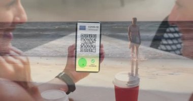 Elinde QR kodlu bir akıllı telefon olan bir kadın plajda yürüyen beyaz bir kadına karşı. covid-19 aşı sertifikası ve sağlık kartı konsepti