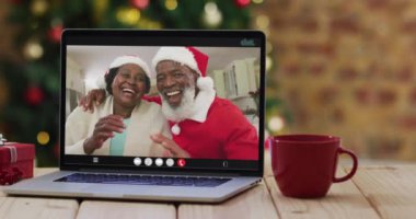 Laptop 'ta Noel Baba şapkası takan Afrikalı son sınıf öğrencisi çiftin Noel ağacı var. Noel, şenlik ve iletişim teknolojisi dijital kompozit video.