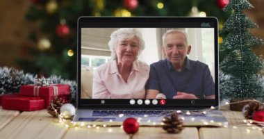 Kafkasyalı son sınıf çifti dizüstü bilgisayarda Noel ağacıyla el sallıyor. Noel, şenlik ve iletişim teknolojisi dijital kompozit video.