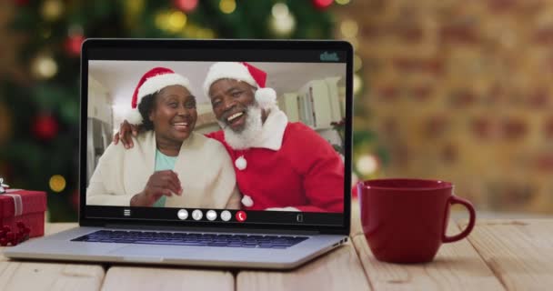 非洲裔美国老年夫妇在笔记本电脑上戴着圣诞帽 带着圣诞圣诞树 带着圣诞礼帽 节日和通信技术数码合成录像 — 图库视频影像
