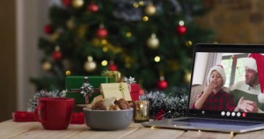 Mutlu baba ve oğul dizüstü bilgisayarlarında Noel süslemeleri ve ağaçlarıyla görüntülü arama yapıyorlar. Noel, şenlik ve iletişim teknolojisi dijital kompozit video.