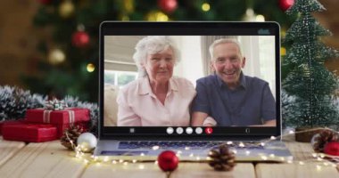 Kafkasyalı son sınıf çifti dizüstü bilgisayarda Noel ağacıyla el sallıyor. Noel, şenlik ve iletişim teknolojisi dijital kompozit video.